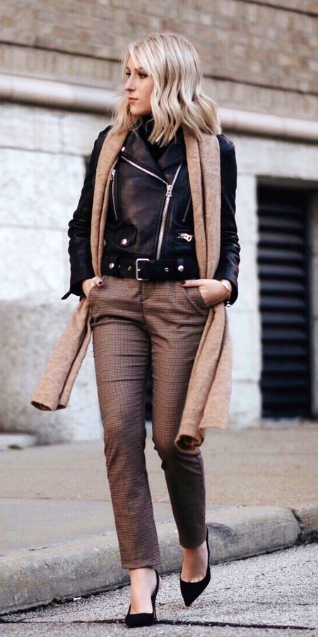 Woman in black leather coat with brown scarf and brown pants walking on road.