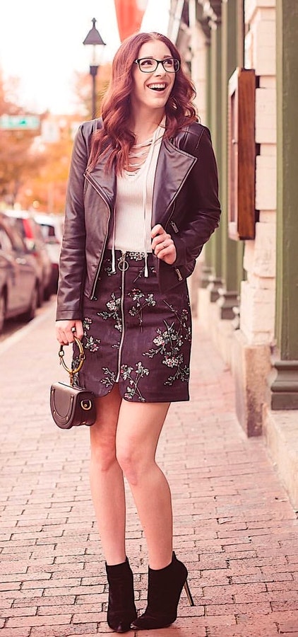 Woman wearing black leather jacket and black skirt near sidewalk.