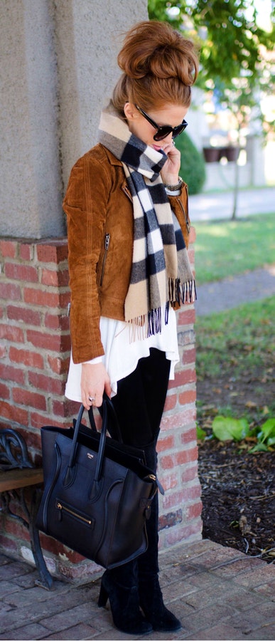 Woman wearing brown jacket with black, white, and gray plaid scarf and black pants carrying black leather two-way bag.