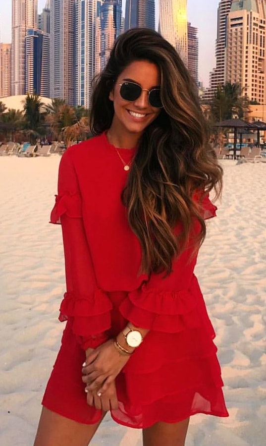 Woman wearing red long-sleeved mini dress standing on sand.