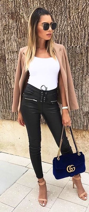 Woman in white tank top standing while holding blue Gucci handbag.