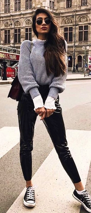 Woman wearing black sunglasses, gray sweater, black leggings, and pair of black lace-up casual sneakers.