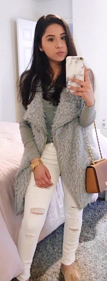 Woman with grey fur coat and distress white denim jeans talking selfie.