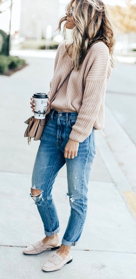 Women's beige sweater, distressed faded blue jeans, and beige shoes.