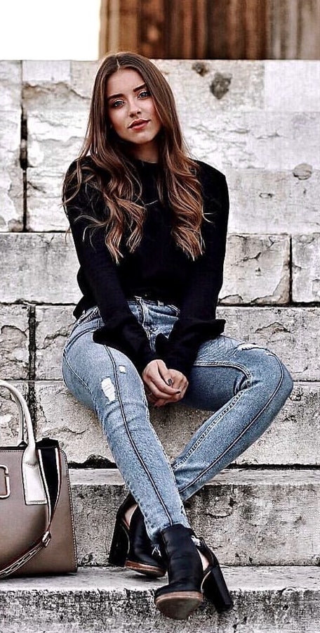 Women's black crew neck long sleeve shirt and distressed blue jeans.