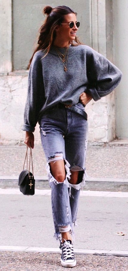 Women's gold-colored sunglasses, gray sweater, faded blue distressed jeans, and blue-and-white low top sneakers.