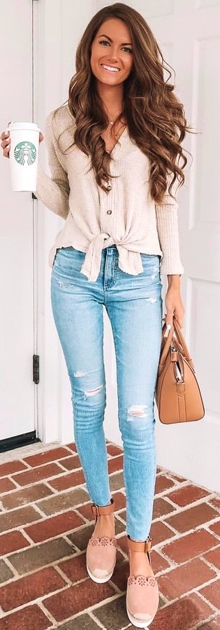 Woman holding Starbucks tumbler and carrying brown bag standing near white wooden door.