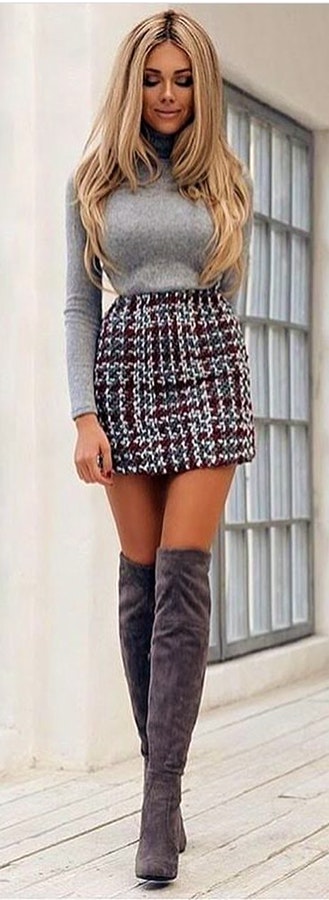 Woman in gray long-sleeved shirt, white and brown knitted mini skirt with pair of gray thigh-high heeled boots.