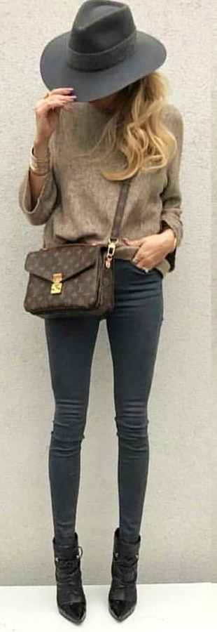 Woman on brown long-sleeved shirt and black hat standing near white wall.