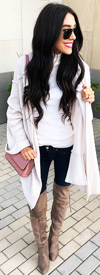 Woman wearing gray cardigan and knee high boots with sling bag.