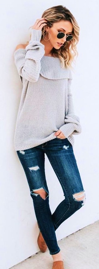 Woman wearing gray off-shoulder sweater and distressed blue jeans.