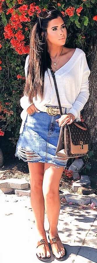 Woman wearing white v-neck long-sleeved shirt and blue denim skirt near flowers.