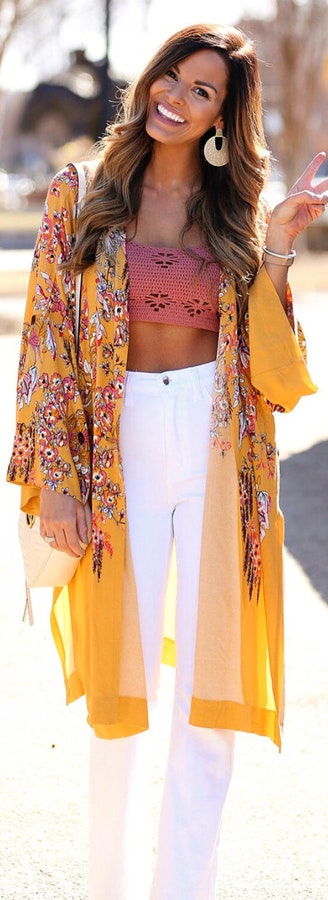 Woman wearing yellow floral cardigan and white pants.