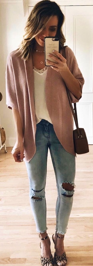 Woman wearing pink cardigan while holding phone.