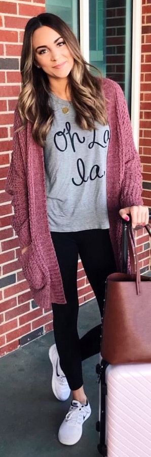 Woman wearing purple long cardigan, gray shirt, black leggings, and black Nike sneakers outfit holding brown leather tote bag.