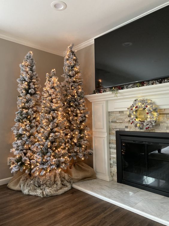 Three flocked Christmas trees next to fireplace.